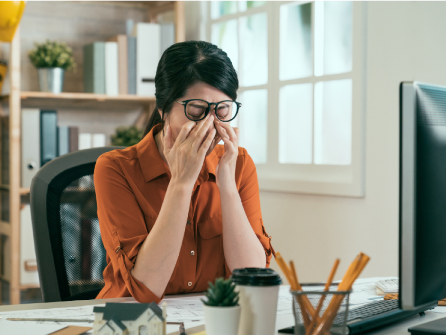 A woman sitting at her desk with her hands covering her face.