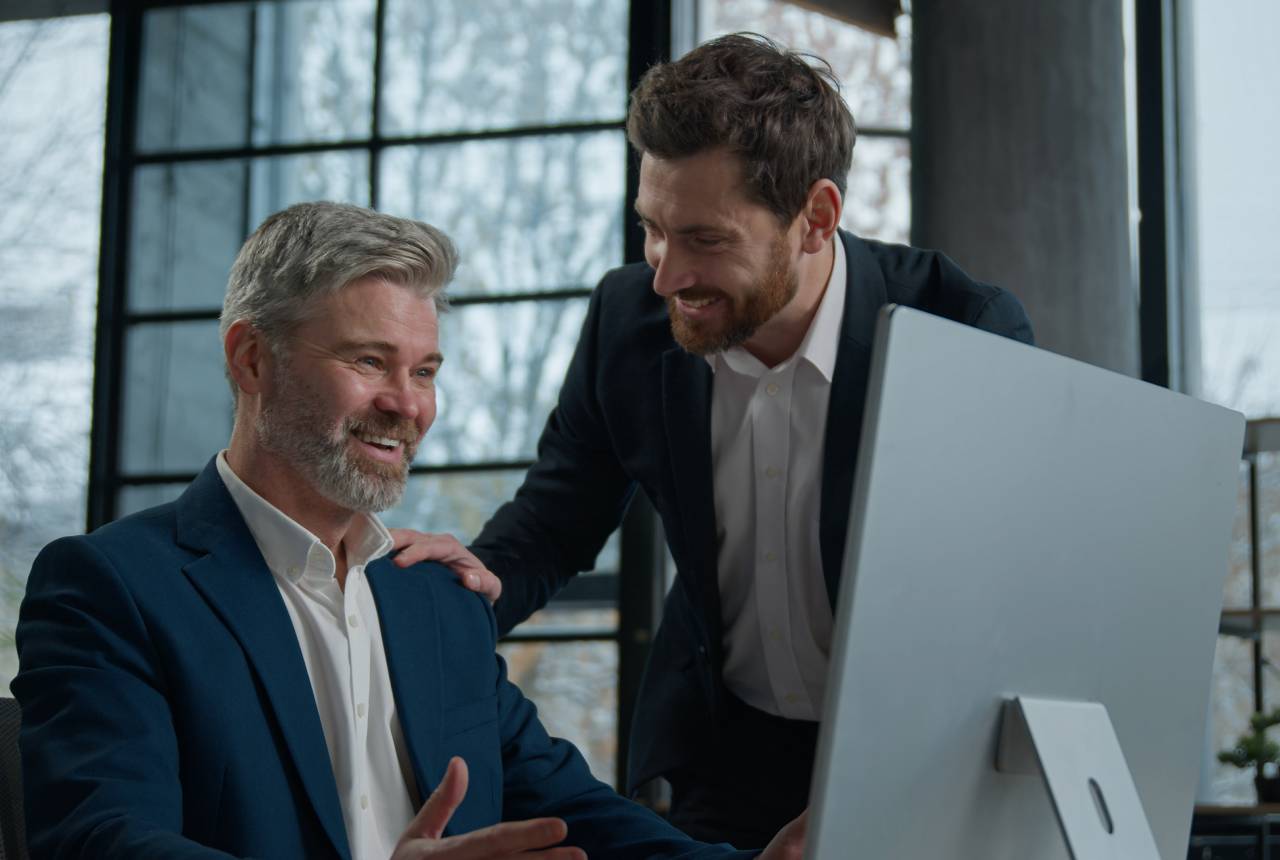 Two men in suits are looking at a computer screen.