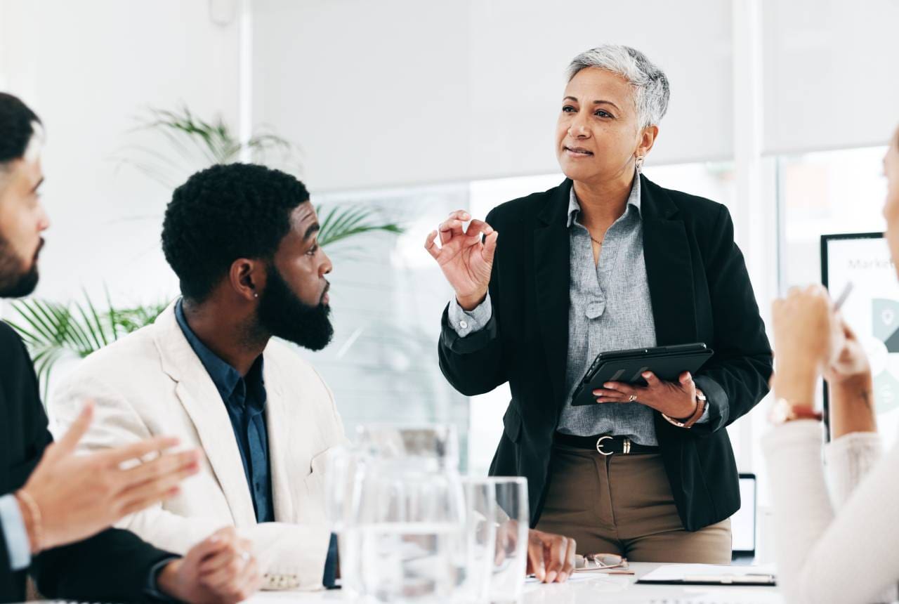 A woman is talking to two men in front of a table.